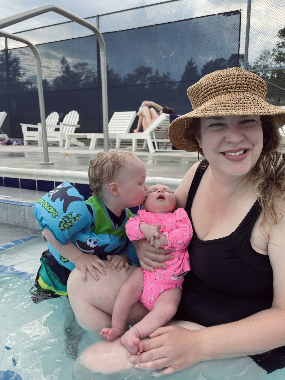 A picture of a mother in a pool, holding a baby with a toddler
