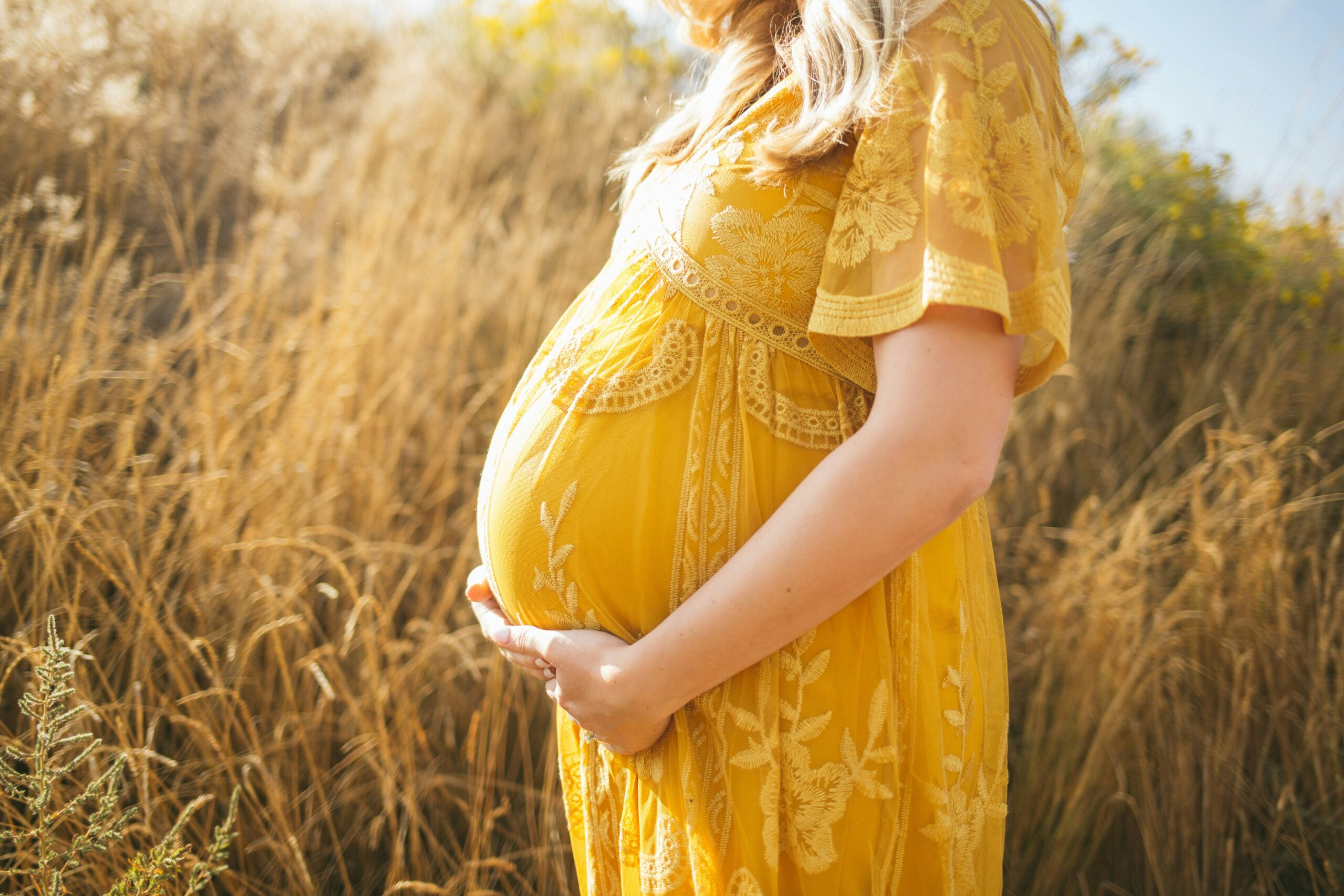 Pregnant woman in yellow dress outside in grass.