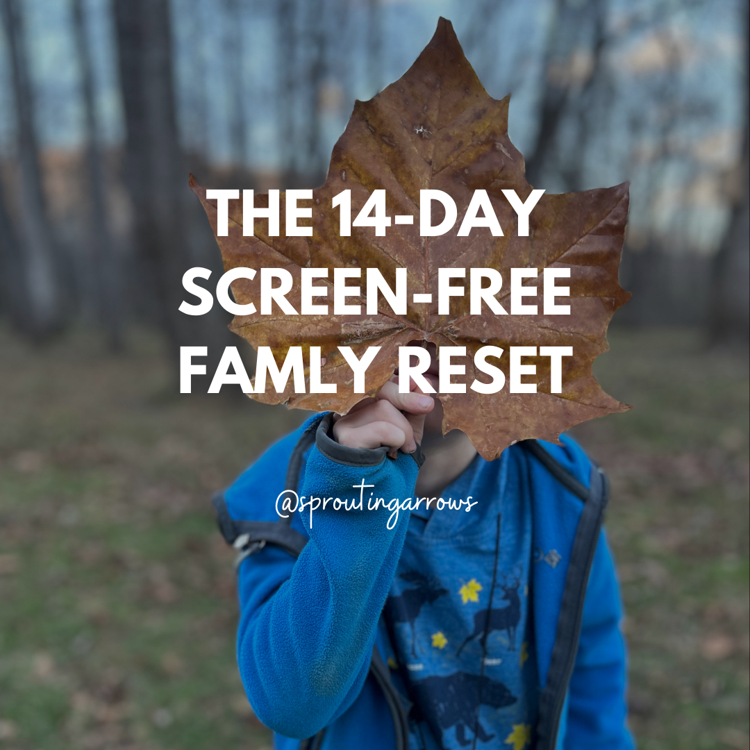 A boy with a large leaf in front of his face outside wearing a blue jacket.